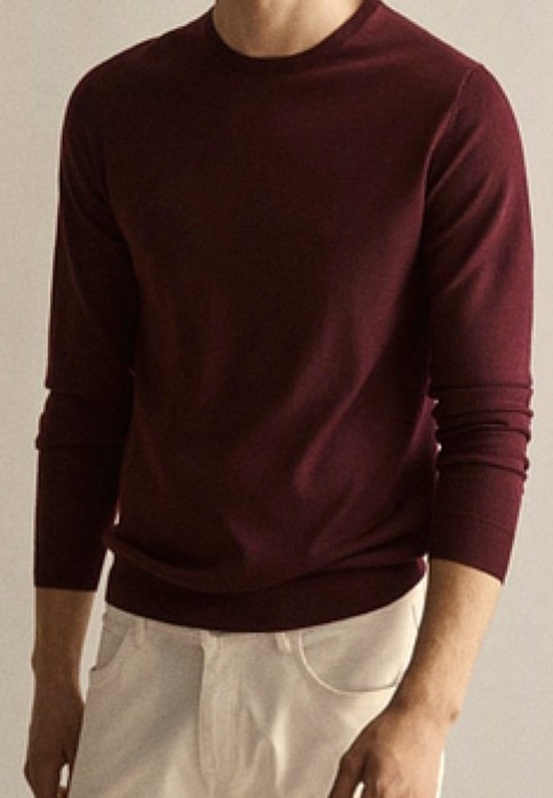 Maglione bordeaux a maniche lunghe realizzato in tessuto morbido, con scollo rotondo e polsini aderenti, abbinato a pantaloni chiari.