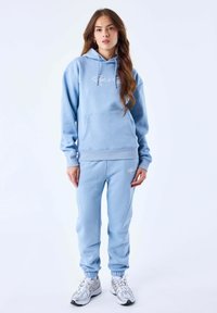 Lichtblauwe hoodie en bijpassende joggers van zacht materiaal; heeft een voorzak en geborduurd logo. Inclusief elastische boorden en tailleband.