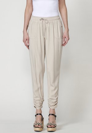 Beige, lehké jogger kalhoty s elastickým pasem, šňůrkou a bočními kapsami; na kotnících stažené manžety; jemná textura látky.