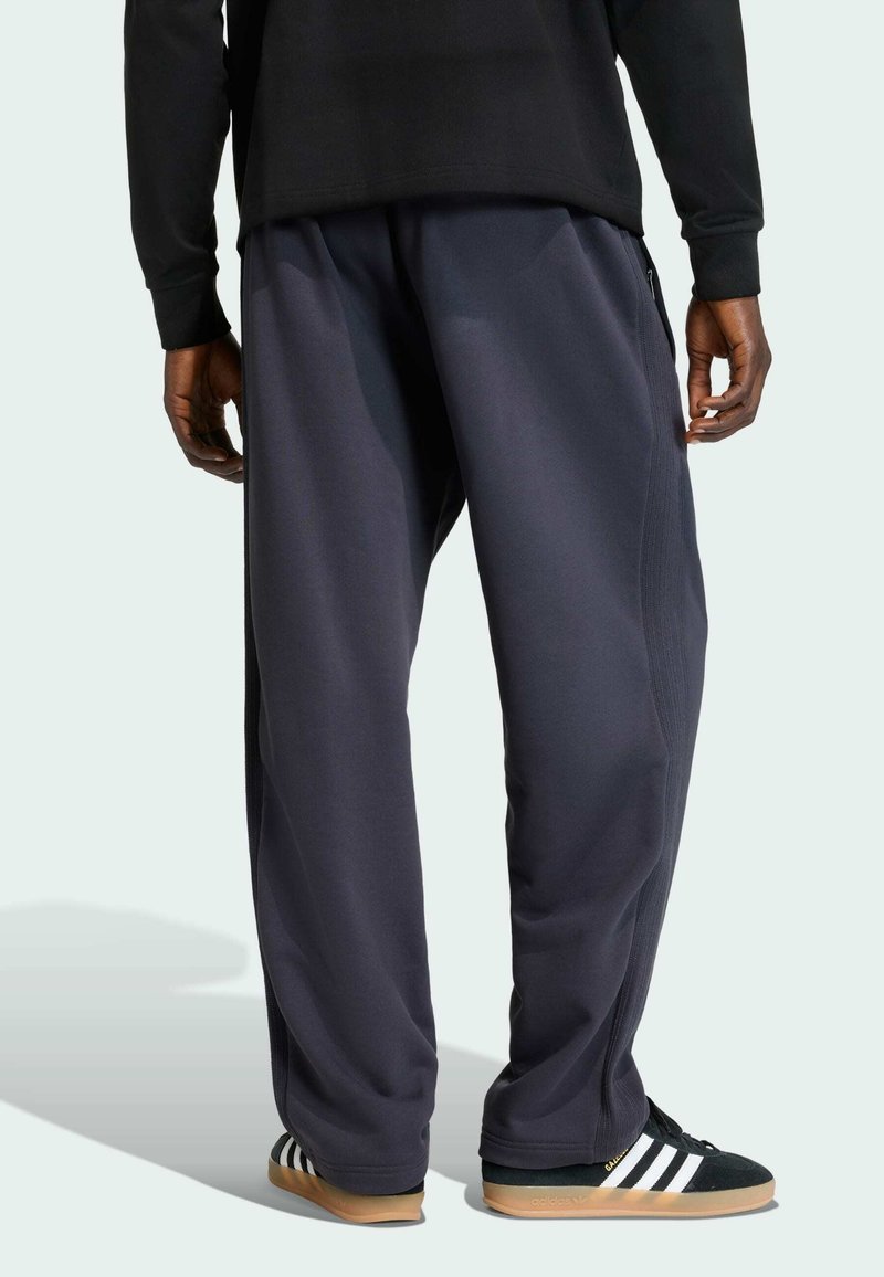 Mørkegrå joggingbukser med bred benudformning, udstyret med lynlåse i siden og tekstureret stof. Kombineret med sorte og hvide sneakers.