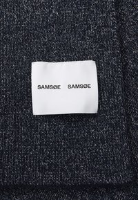 Tessuto a maglia blu navy con una texture morbida. Un'etichetta bianca mostra "SAM SøE SAM SøE" in grassetto nero, attaccata al tessuto.