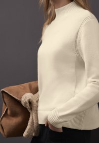 Krémový svetřík s žebrovaným límcem a bočními detaily, doplněný hnědou texturovanou kabelkou. Hladká pletenina, přiléhavý střih.