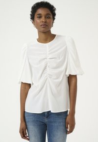 Top bianco a maniche corte con dettagli arricciati davanti, collo rotondo, realizzato in tessuto morbido, indossato con jeans blu.
