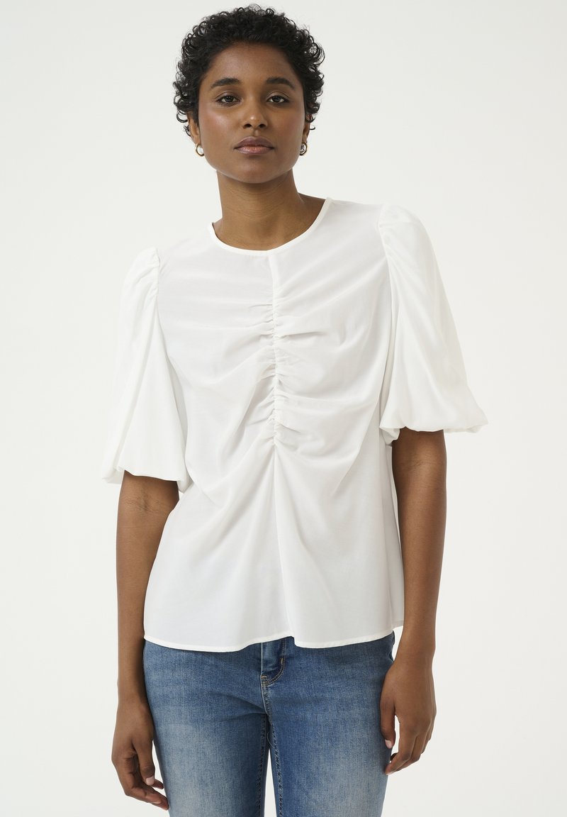 Top bianco a maniche corte con dettagli arricciati davanti, collo rotondo, realizzato in tessuto morbido, indossato con jeans blu.
