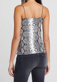 Svartvit ormskinsmönstrad topp med tunna axelband, figurnära design, slät textur och en något kortare nederkant, kombinerad med mörka jeans.