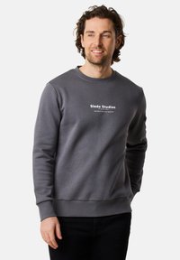 Felpa grigia con collo rotondo, polsini e orlo a coste. Presenta la scritta bianca "Slade Studios" sul petto. Tessuto morbido, design casual.