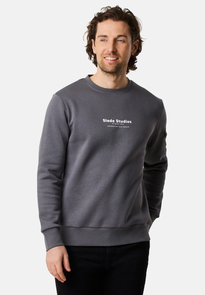 Felpa grigia con collo rotondo, polsini e orlo a coste. Presenta la scritta bianca "Slade Studios" sul petto. Tessuto morbido, design casual.