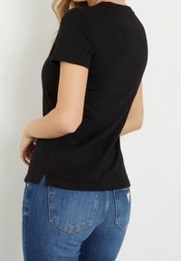 Camiseta negra de manga corta con un diseño ajustado, con un escote redondo y una abertura lateral en el dobladillo, combinada con unos jeans de mezclilla azules.