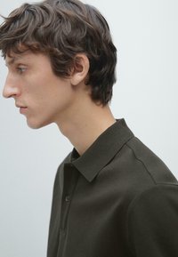 Ciemnozielona koszulka polo z kołnierzykiem i dwoma guzikami, wykonana z gładkiej, teksturowanej tkaniny i o dopasowanym kroju.