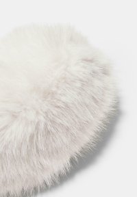 Coussin en fausse fourrure blanche de forme ronde, doté de fibres longues et douces ainsi que d'une texture moelleuse. Aucune quincaillerie ou motif visible.