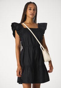 Rochie din bumbac neagră cu mâneci volan, decolteu pătrat, talie îngustată și fustă evazată. Asortată cu o geantă crossbody de culoare crem.