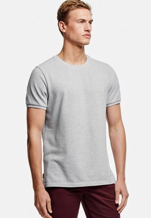 Grijze katoenen t-shirt met een ronde hals, korte mouwen en een textuurafwerking; gecombineerd met donkerrode broeken. Geen zichtbare logo's of graphics.