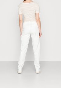 Pantalon en coton blanc avec une coupe décontractée et des jambes fuselées, associé à un haut à rayures léger à manches courtes. Chaussures simples.