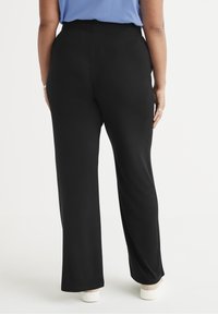Zwarte, wijde broek met een elastische tailleband, gemaakt van een gladde, zachte stof en met een eenvoudig ontwerp. Lichte rimpeling aan de achterkant.