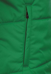 Sezione di giacca a vento verde con una cerniera a contrasto. Il tessuto appare liscio con una finitura leggermente texturizzata e un design trapuntato.