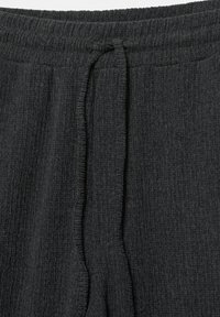 Közeli kép sötét szürke bordázott kötött nadrágról, rugalmas derekkal és elöl középen elhelyezett húzózsinórral.