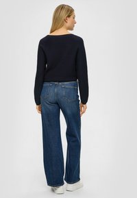 Klassischer marineblauer Pullover mit weitem Ausschnitt, kombiniert mit hoch geschnittenen, locker sitzenden dunklen Denim-Jeans und weißen Plateausneakern.
