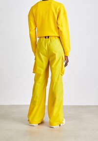 Geel sweatshirt met raglanmouwen gecombineerd met bijpassende lichtgewicht cargobroek met zakken. Soepele textuur, relaxte pasvorm.
