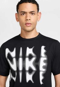 Zwart T-shirt met korte mouwen met een witte vervormde tekst grafische ontwerp. De stof lijkt glad en lichtgewicht. Geen opmerkelijke hardware of accenten.