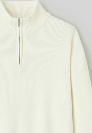 Pull en tricot côtelé crème avec un col à fermeture éclair partielle et des manches longues, présenté sur un fond clair uni.