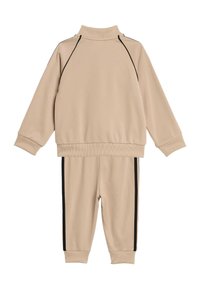 Beige treningsdress laget av mykt materiale; har høy krage, lange ermer og svarte sidestriper på buksen og toppen.