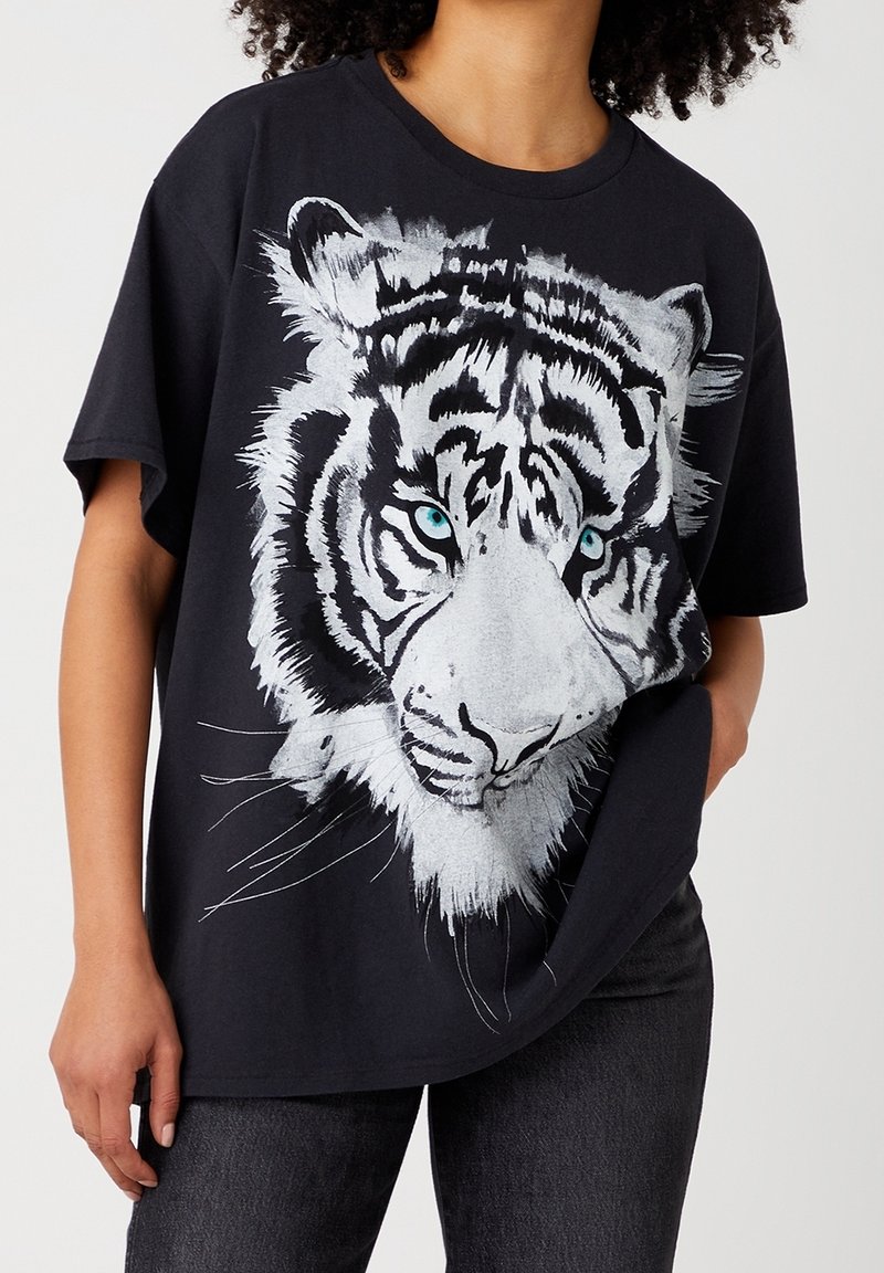 Musta puuvillapaita, jossa on suuri valkoinen tiikeri -grafiikka sinisillä silmillä, lyhyet hihat ja rento istuvuus.