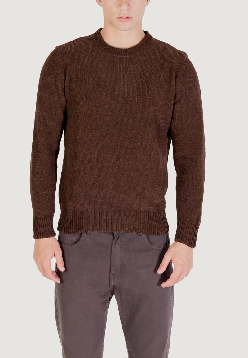 Maglione a maglia marrone con texture, scollo rotondo e polsini a coste, abbinato a pantaloni grigi, che mostrano un design aderente.