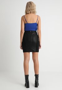 Sinisen ohutolkaimisen toppi yhdistettynä mustaan keinonahkaiseen minihameeseen, jossa on takazippari ja taskut. Mukana mustat nilkkurit korkokorolla.