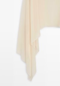 Flødefarvet stof med bløde, flydende folder, der hænger i lagdelte, ujævne spidse former mod en hvid baggrund.