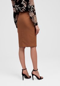 Brąskowa spódnica ołówkowa wykonana z elastycznego materiału, cechująca się dopasowanym krojem i gładką fakturą, w połączeniu z czarnymi sandałami na wysokim obcasie.