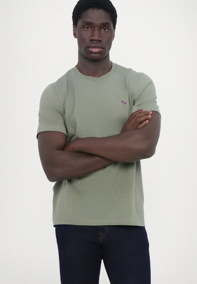 Felsőtesthez tapadó, crew-neck póló olíva zöld pamutból, rövid ujjakkal. A bal felső mellrészen egy apró hímzett logóval rendelkezik.