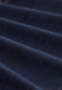 Tamnavo jeans tkanina s glatkom teksturom, koja sadrži vidljive bijele točkice. Materijal je presavijen u nekoliko slojeva, pokazujući suptilan sjaj.