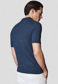Granatowa koszulka polo z krótkim rękawem, wykonana z teksturowanej dzianiny. Dopasowany krój z prążkowanym wykończeniem dołu i kołnierza. Tylny widok ukazuje szwy na ramionach i gładki materiał.