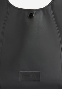 Bolso de mano de cuero negro con un diseño curvado, superficie texturizada y un botón de presión negro brillante. Incluye un parche con el logo en la parte frontal.