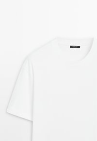 White cotton t-shirt with short sleeves, featuring a round neckline and a black label at the collar. Smooth texture, minimal design.