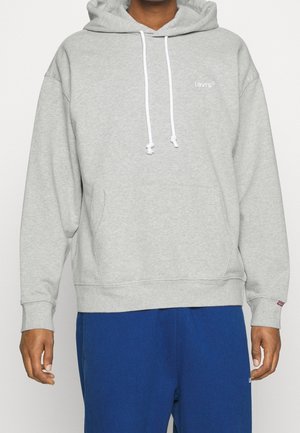 Sudadera de felpa gris con un bolsillo frontal, cordones blancos y pequeño logo de Levi's en el pecho. Puños y dobladillo de canalé. Se lleva con pantalones azules.