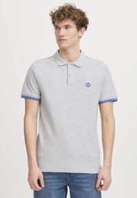 Polo shirt gris clair avec un design uni, des accents bleus sur le col et les manches, et un petit logo bleu sur la poitrine. Manches courtes.