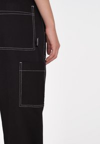 Czarne spodnie z białymi szwami, wieloma dużymi kieszeniami i metką Volcom z boku. Materiał ma mocną teksturę.