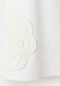 Tissu côtelé blanc avec une grande applique ronde en crochet blanc texturé cousue près du bord.
