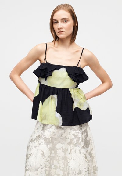 Μαύρο και ανοιχτό πράσινο φλοράλ τοπ με βολάν, λεπτές τιράντες και ζωνάκι με πιέτες, συνδυασμένο με μια υφασμάτινη ασημένια φούστα.