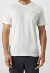 Camiseta de algodón blanca de manga corta, con un logo de Nike naranja en el pecho. Diseño sencillo, cuello redondo, textura suave.