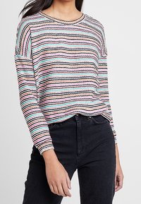Sweter w paski z dzianiny w pastelowych kolorach, z okrągłym dekoltem, długimi rękawami i luźnym krojem. Materiał wydaje się strukturalny i miękki.