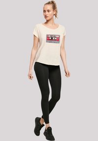 Cream-colored t-shirt with a graphic of a cassette tape; paired with black leggings and black athletic shoes. Casual, relaxed fit.