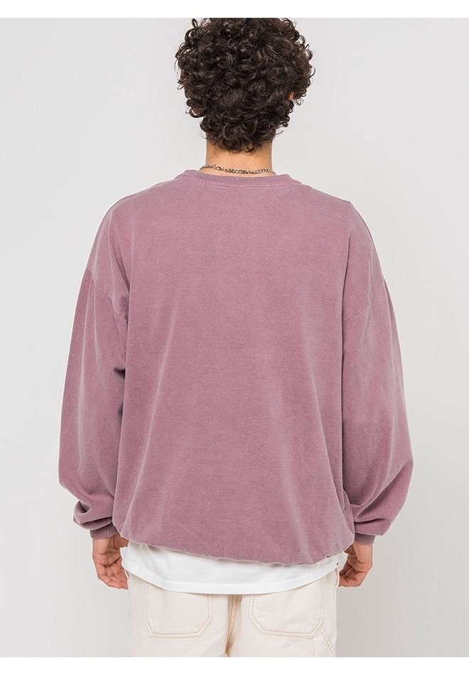 Personne aux cheveux bouclés porte un t-shirt mauve à manches longues ample et délavé par-dessus un t-shirt blanc, tournée de dos sur un fond uni.