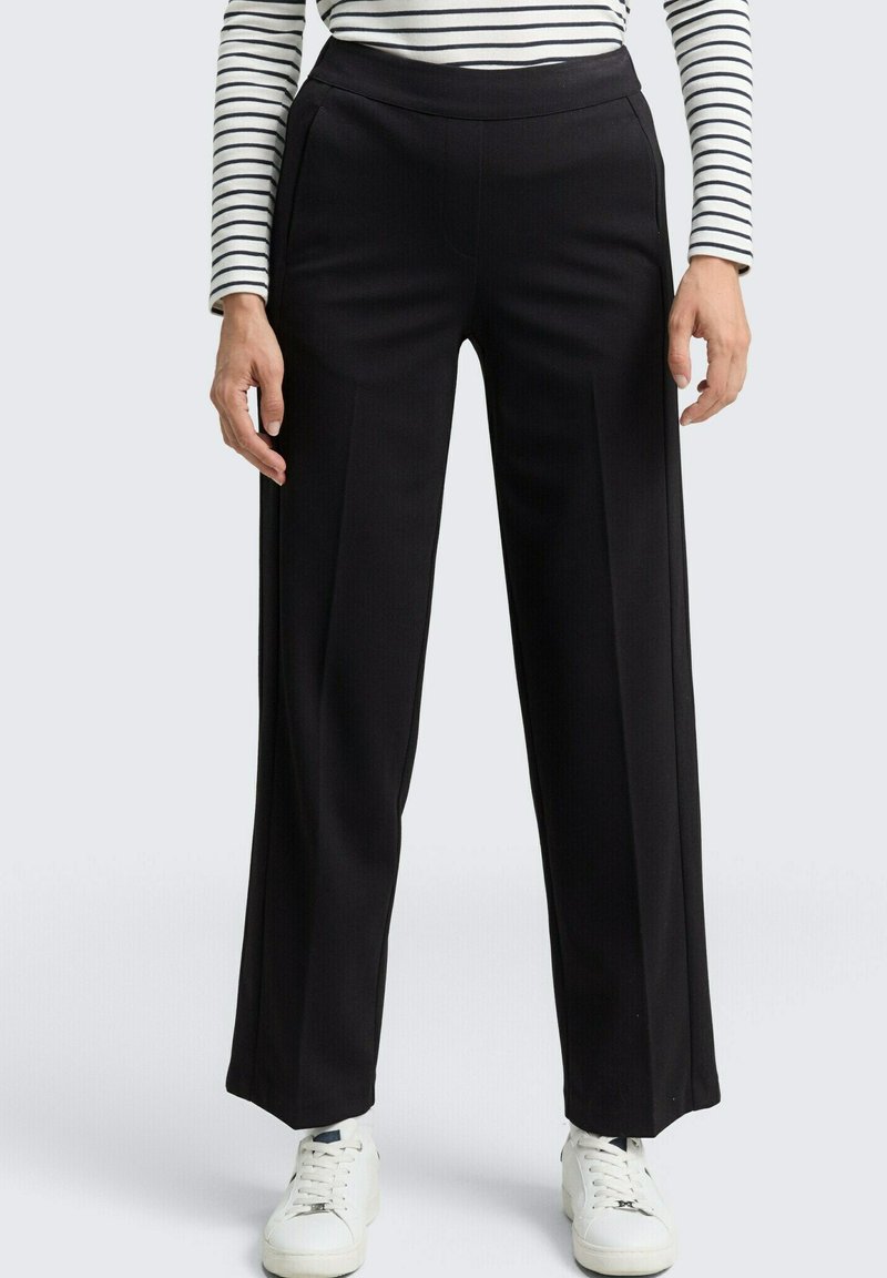 Zwarte wijde broek heeft een gladde textuur, hoge tailleband en voorplooien. Gecombineerd met een gestreept top en witte sneakers.