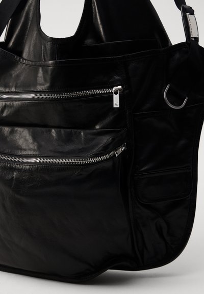 Sort læder skuldertaske med flere lynlås-lommer, tekstureret overflade og justérbar rem; har sølvfarvede hardware-detaljer.