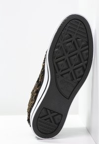 Černá gumová podešev tenisky s texturovaným gripem. Má bílý okraj podél okraje a chlupatý, hnědý svrchní materiál.