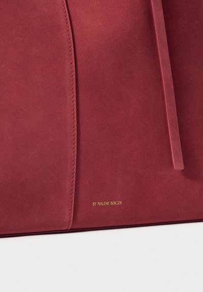 Suede handbag in deep red featuring a smooth texture, subtle stitching, and a gold logo "BY MALENE BIRGER" near the bottom.