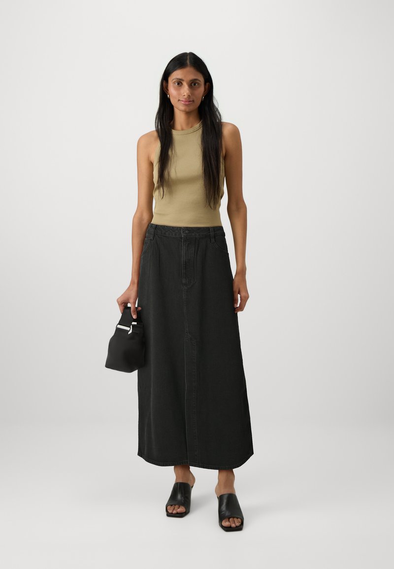 Beiger ärmelloser Oberteil, schwarze Denim-Maxiröcke, schwarze Leder-Mules mit offenem Zeh und eine kleine schwarze Tasche. Schlichtes, tailliertes Design mit minimalen Akzenten.