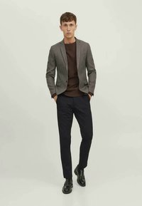 Gråternet blazer over en brun skjorte, parret med mørke bukser og sorte sko. Blazeren har en skræddersyet pasform og notch lapels.